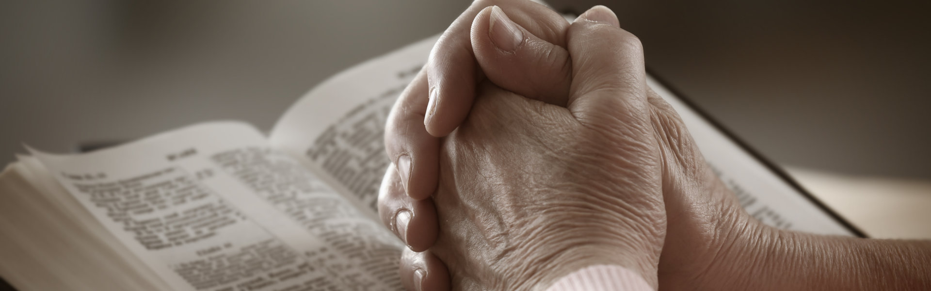 Hands of old woman with Bible on table